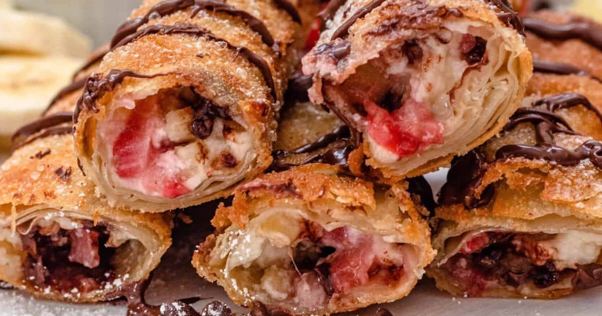 Close-up of crispy dessert rolls filled with cream, strawberries, and chocolate, drizzled with chocolate sauce.