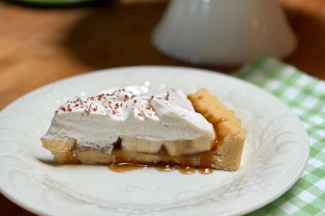A slice of banoffee pie with whipped cream and caramel sauce on a white plate.