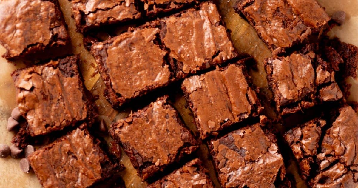Squares of fudgy brownies with cracked tops arranged on parchment paper.