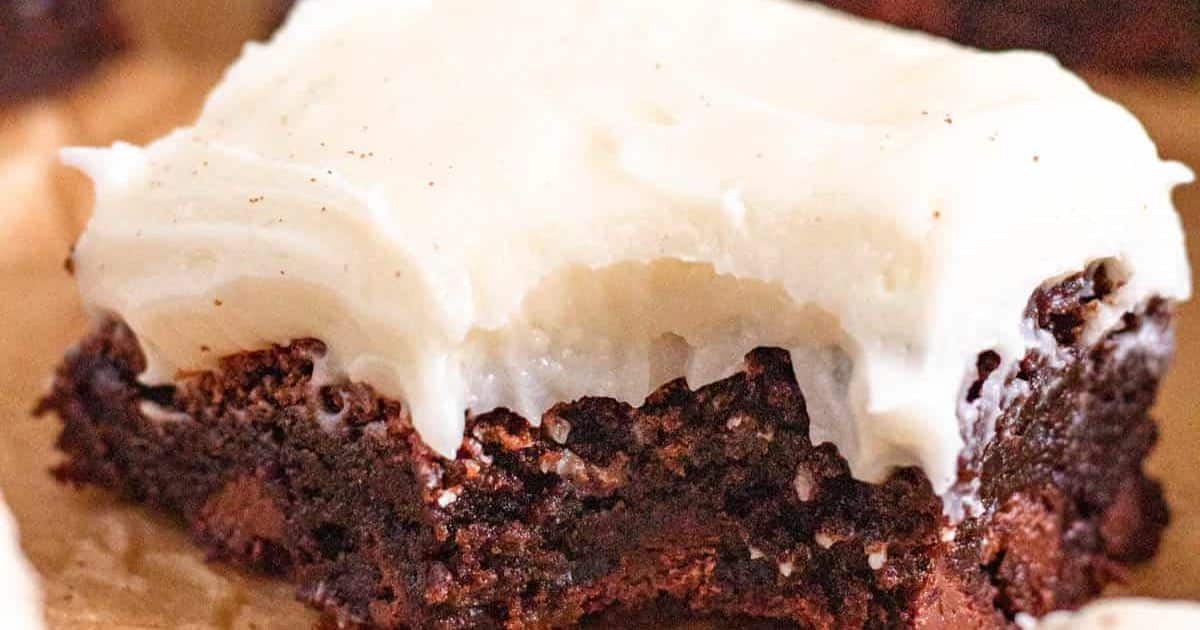 A close-up of a chocolate brownie topped with a thick layer of creamy white frosting.