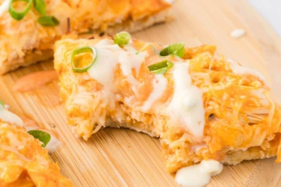 A slice of buffalo chicken pizza with melted cheese, green onions, and white sauce on a wooden board.