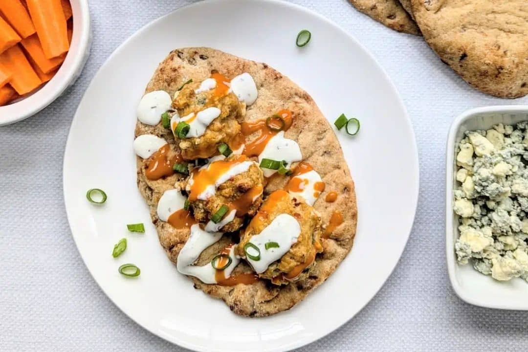 Flatbread with three buffalo chicken meatballs, ranch, hot sauce, and green onions on a white plate.
