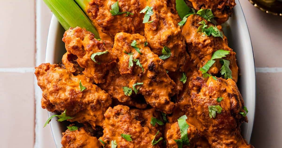 A bowl of saucy buffalo chicken wings garnished with cilantro, served with celery sticks.