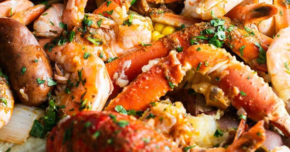 Closeup of a seafood boil with crab legs, shrimp, sausage, corn, and parsley garnish.