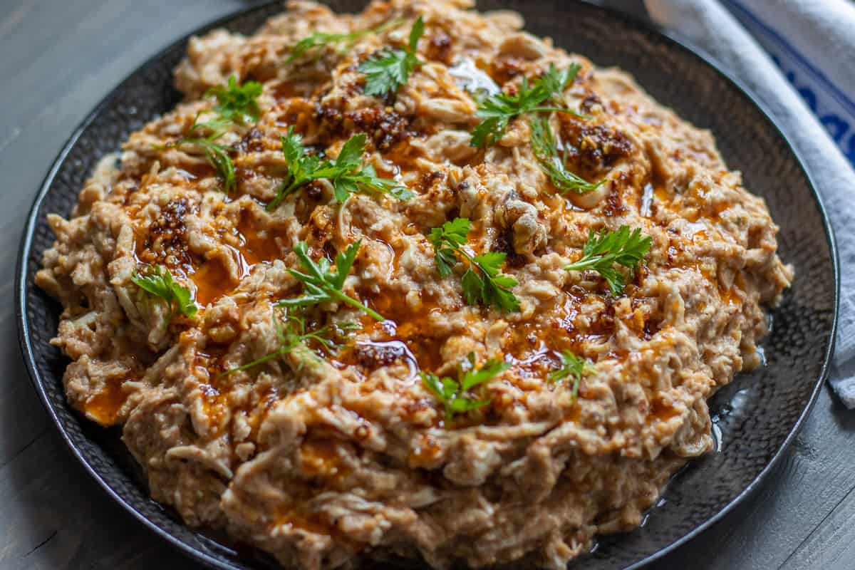 Shredded chicken in a creamy sauce, garnished with fresh herbs and a drizzle of red oil on a dark plate.