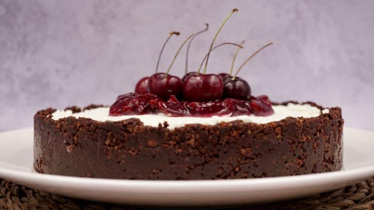 Chocolate cheesecake topped with cherries and cherry sauce on a white plate against a light background.
