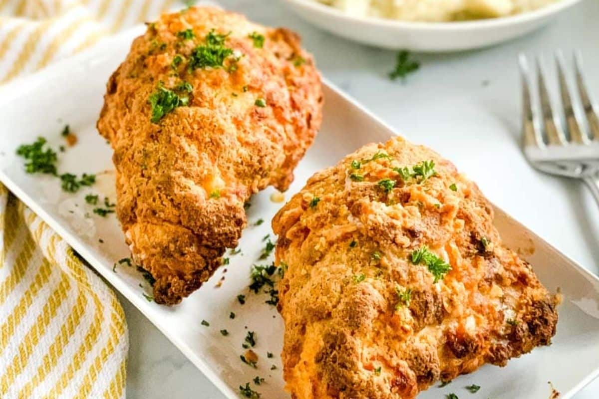Two pieces of golden fried chicken garnished with parsley on a white rectangular plate.