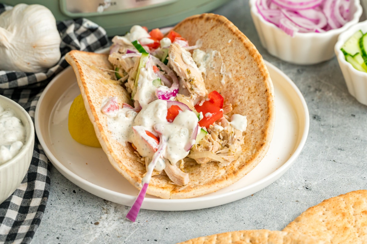 A pita stuffed with shredded chicken, diced tomatoes, onions, cucumber, and white sauce on a plate.