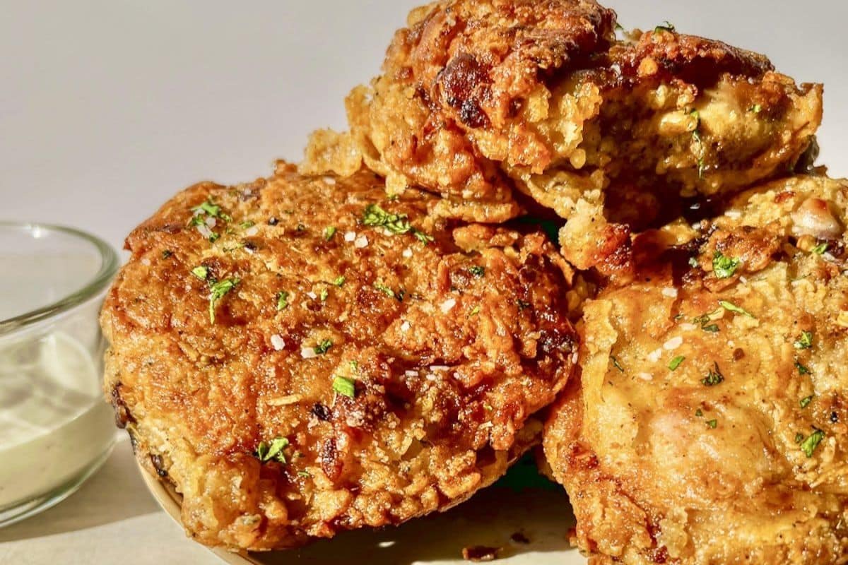 Golden, crispy fried chicken pieces garnished with herbs, next to a small bowl of dipping sauce.