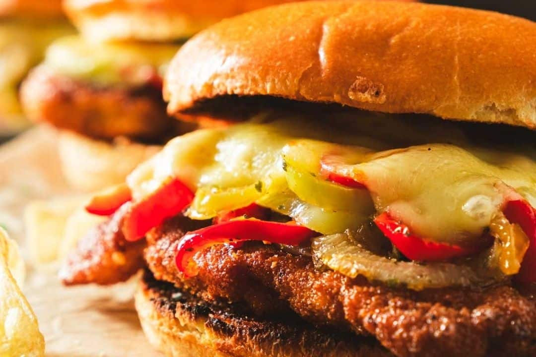 Close-up of a sandwich with melted cheese, grilled chicken, and sautéed peppers on a toasted bun.