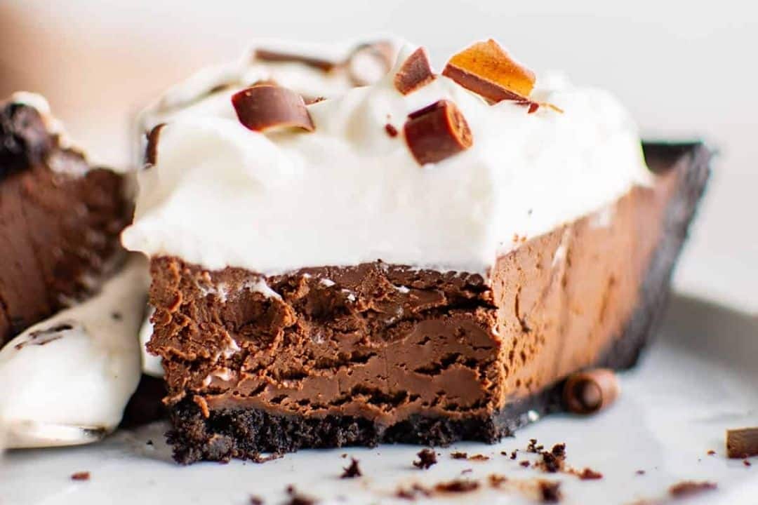 A close-up of a chocolate cream pie slice with whipped cream and chocolate shavings on top.