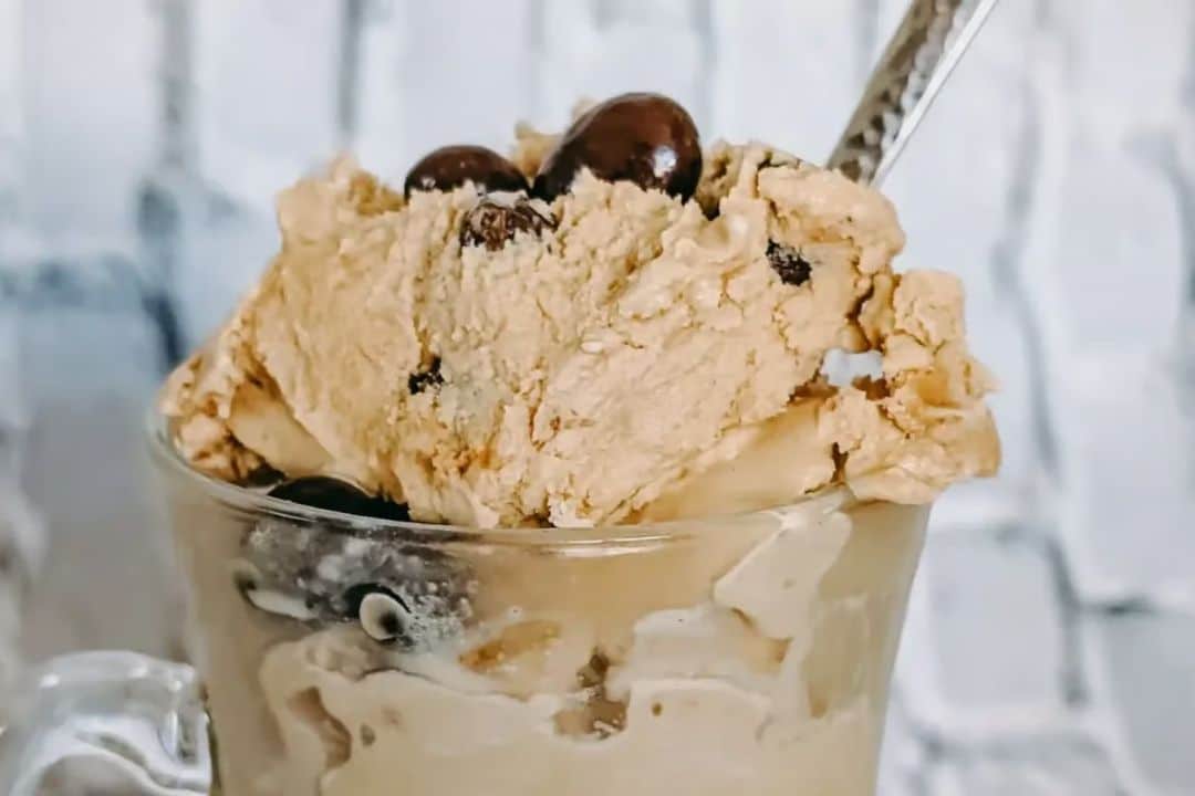 A glass mug filled with creamy coffee ice cream and chocolate-covered coffee beans, with a spoon inside.