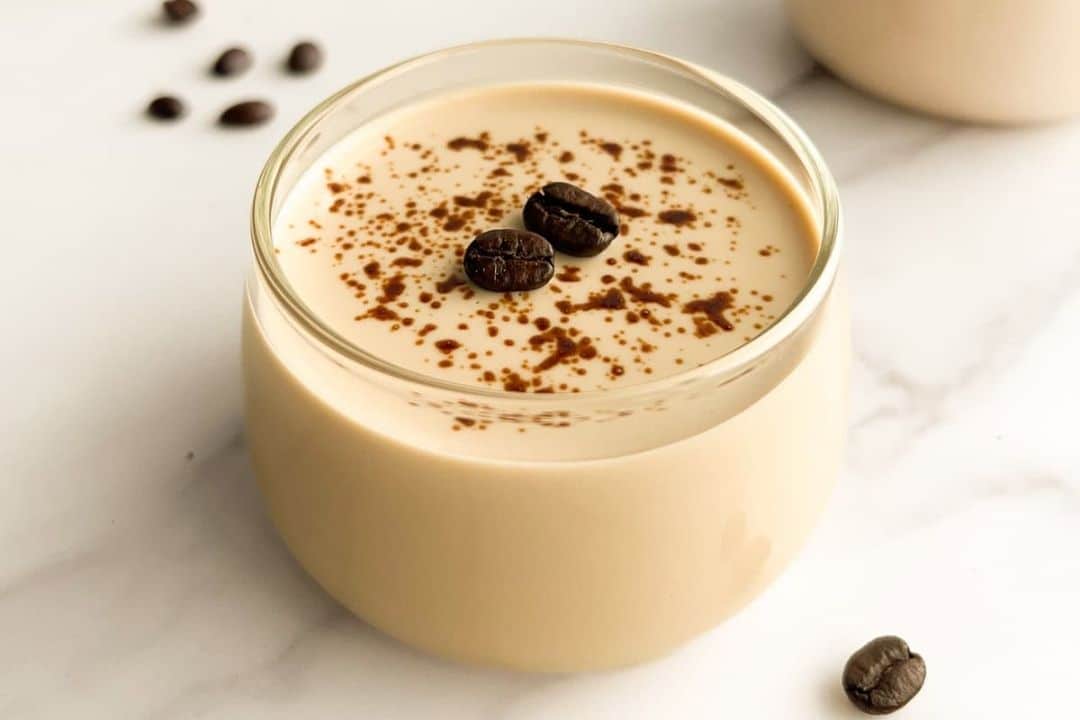 A creamy coffee dessert in a glass jar, topped with coffee beans and a sprinkle of cocoa powder.