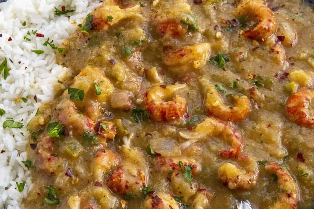 Crawfish étouffée with white rice, garnished with fresh herbs and red pepper flakes.