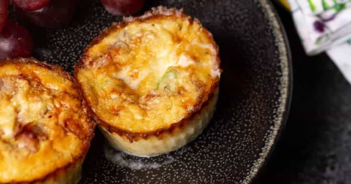 Two mini quiches on a dark plate with a side of red grapes.