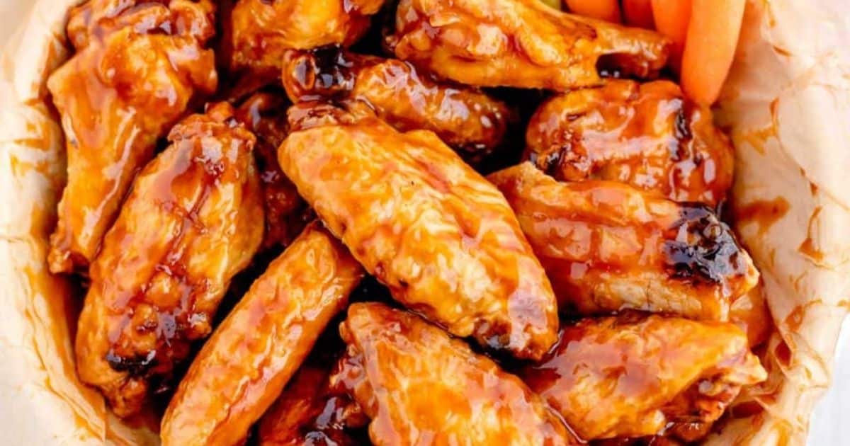A basket of glazed barbecue chicken wings with a few baby carrots in the corner.