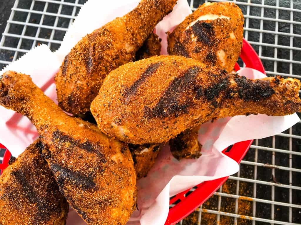 Grilled, seasoned chicken drumsticks in a red basket lined with white parchment paper on a wire rack.