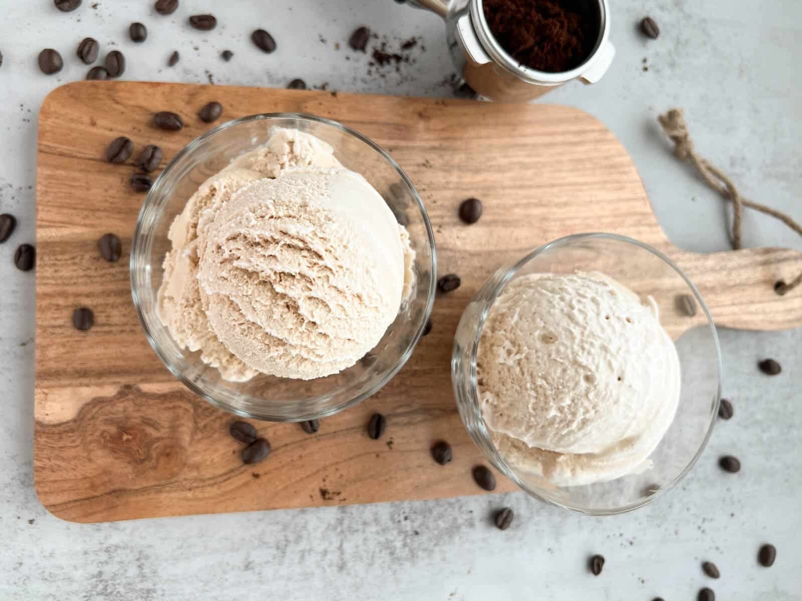 Two glass bowls of coffee ice cream on a wooden board, with coffee beans scattered around.