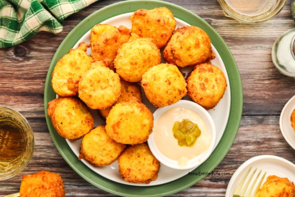 A plate of golden hush puppies with a dipping sauce and relish, on a wooden table.