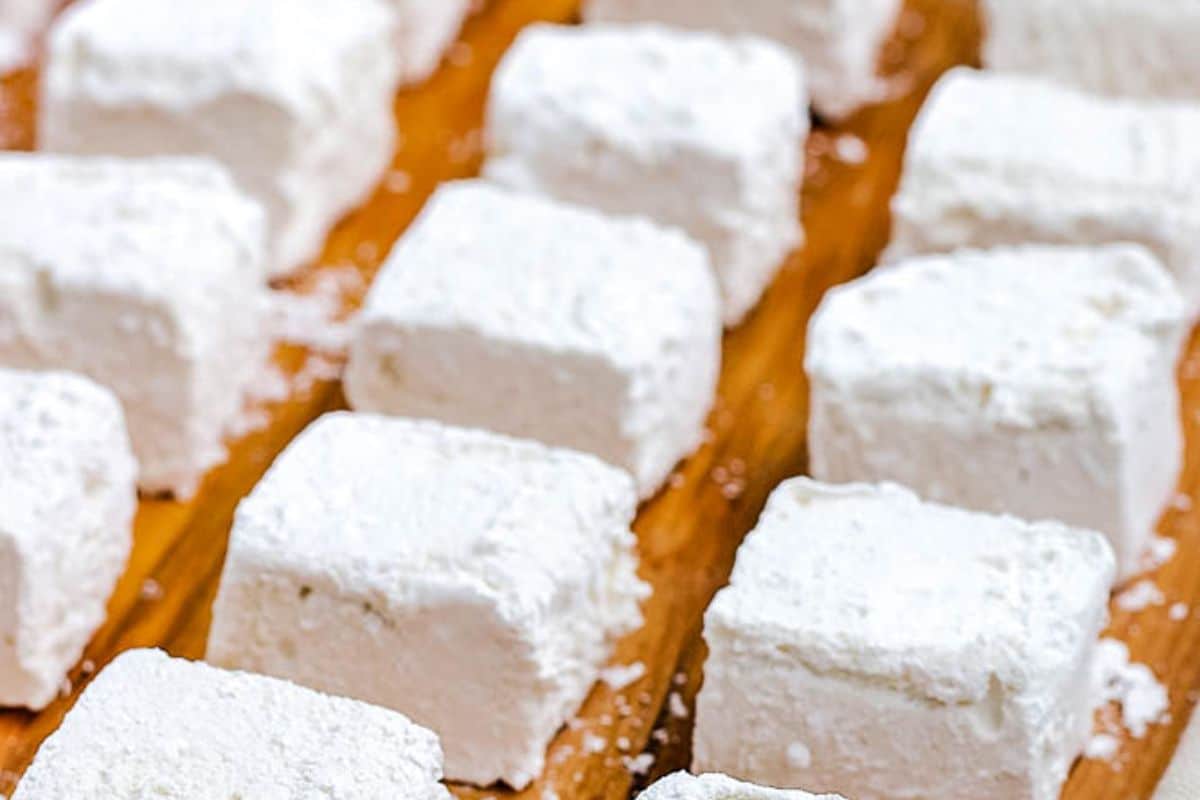 Rows of white, powdered sugar-covered marshmallows on a wooden surface.