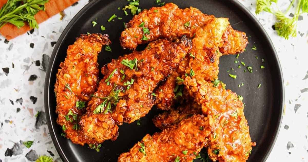 Crispy fried chicken tenders topped with chopped herbs on a black plate.