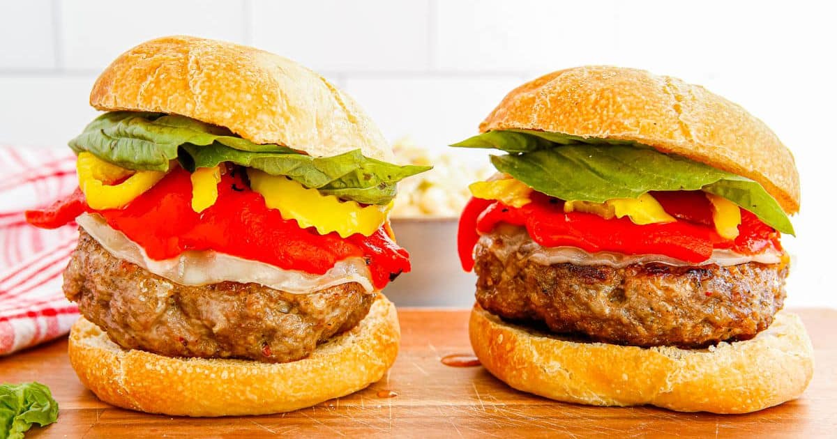Two gourmet burgers with lettuce, cheese, and peppers on buns, set on a wooden board against a white background.