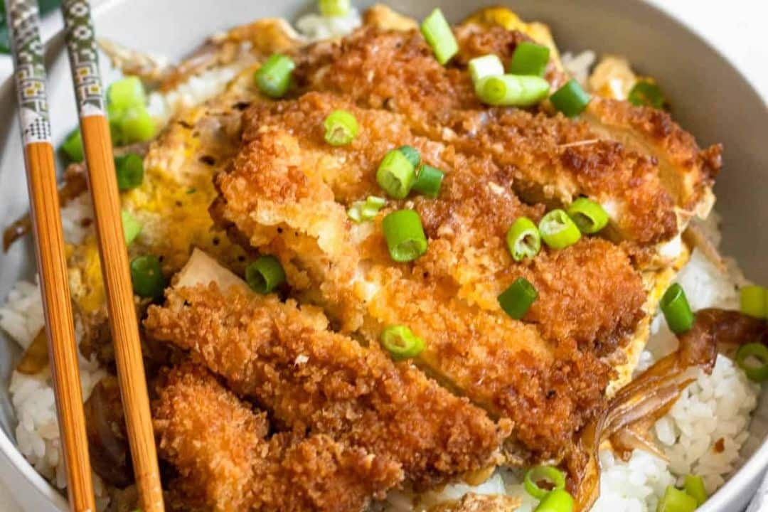 Breaded chicken cutlet on white rice, topped with green onions. Chopsticks rest on the bowl's edge.