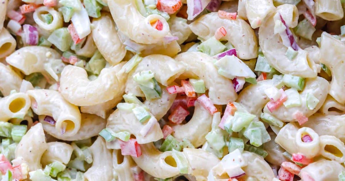 Close-up of macaroni salad with chopped red onion, celery, and bell peppers in a creamy dressing.