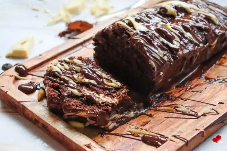 A sliced chocolate loaf cake drizzled with white and dark chocolate on a wooden board.