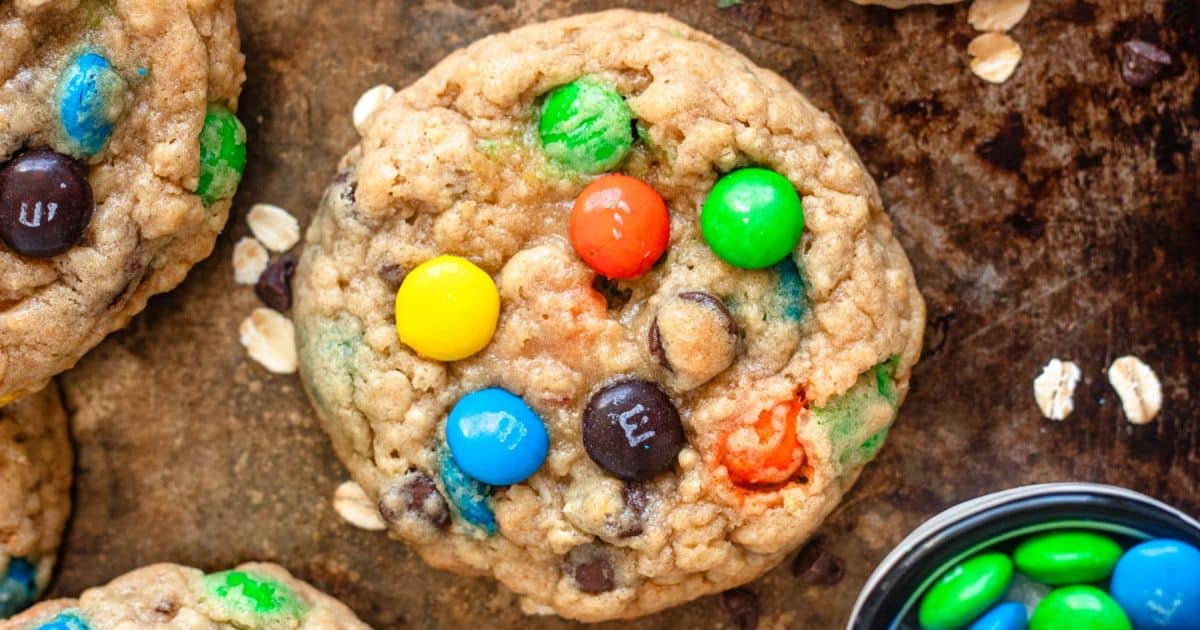 A close-up of an oatmeal cookie with colorful M&M candies on a rustic baking sheet.
