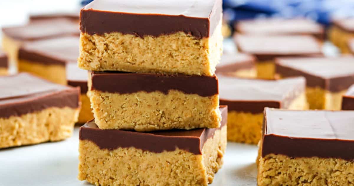 Three stacked peanut butter bars with a chocolate topping, surrounded by more bars on a white surface.