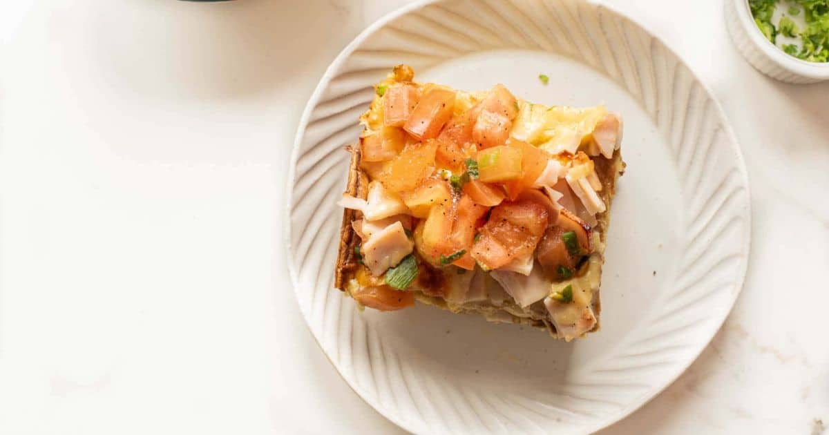 A slice of lasagna topped with chopped tomatoes and herbs on a white plate.