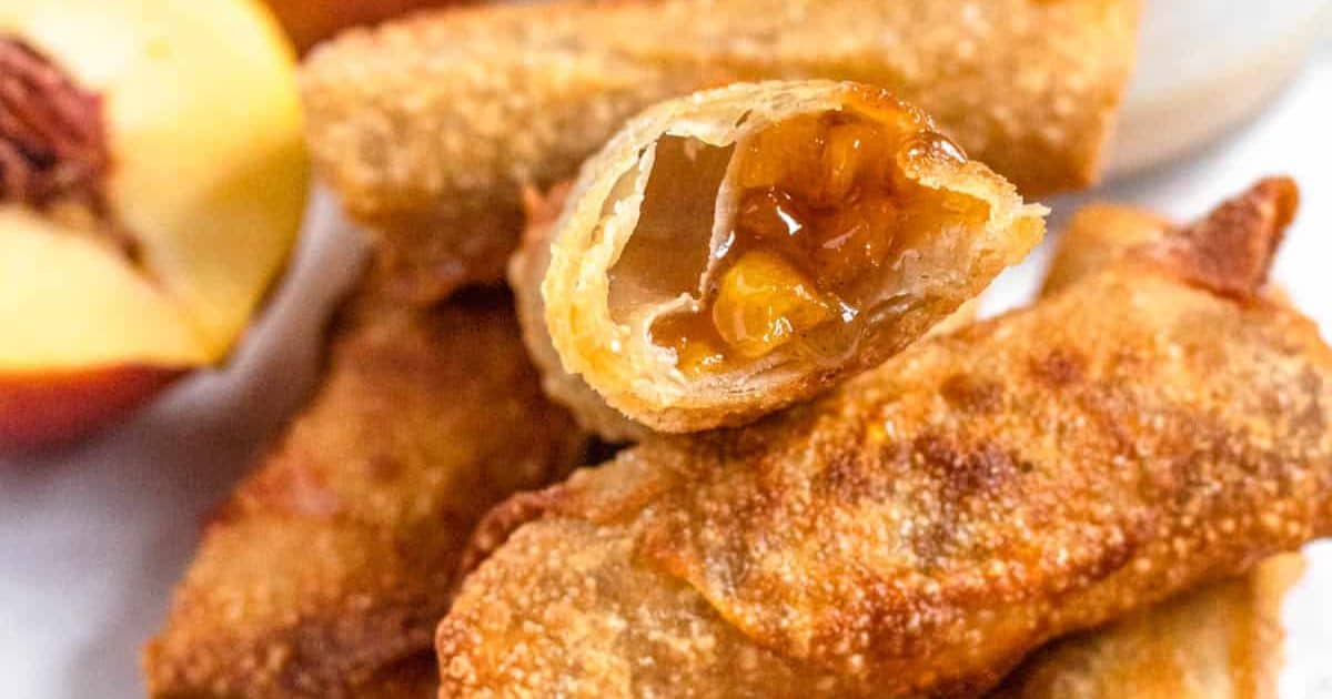 Close-up of crispy peach-filled egg rolls, one broken open to show the juicy peach filling inside.