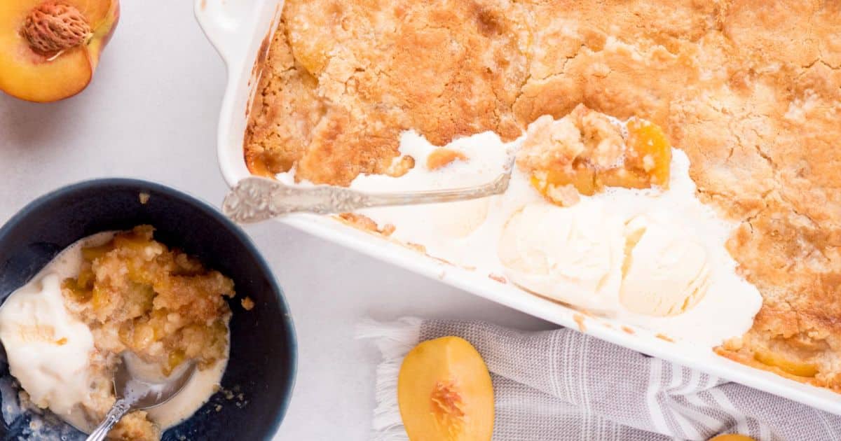 Peach cobbler with ice cream in a baking dish, served in a bowl, with fresh peach slices on the table.