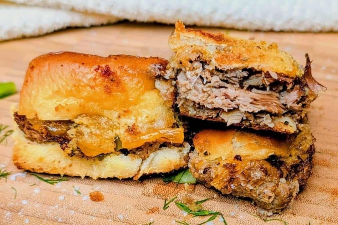 Two halves of a pulled pork sandwich with melted cheese on toasted bread, resting on a wooden surface.