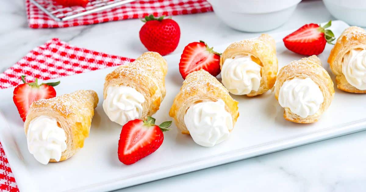 Pastry cream horns with whipped cream filling and fresh strawberries on a white platter.