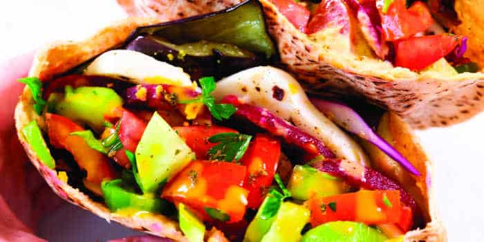 Colorful vegetable pita wraps filled with tomatoes, cucumbers, lettuce, and eggplant, held in a hand.