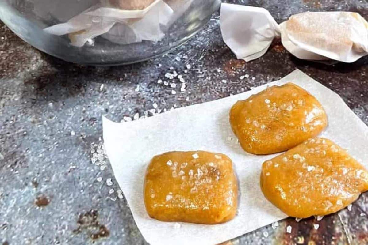 Three pieces of salted caramel candy on parchment paper, with more wrapped caramels in the background.