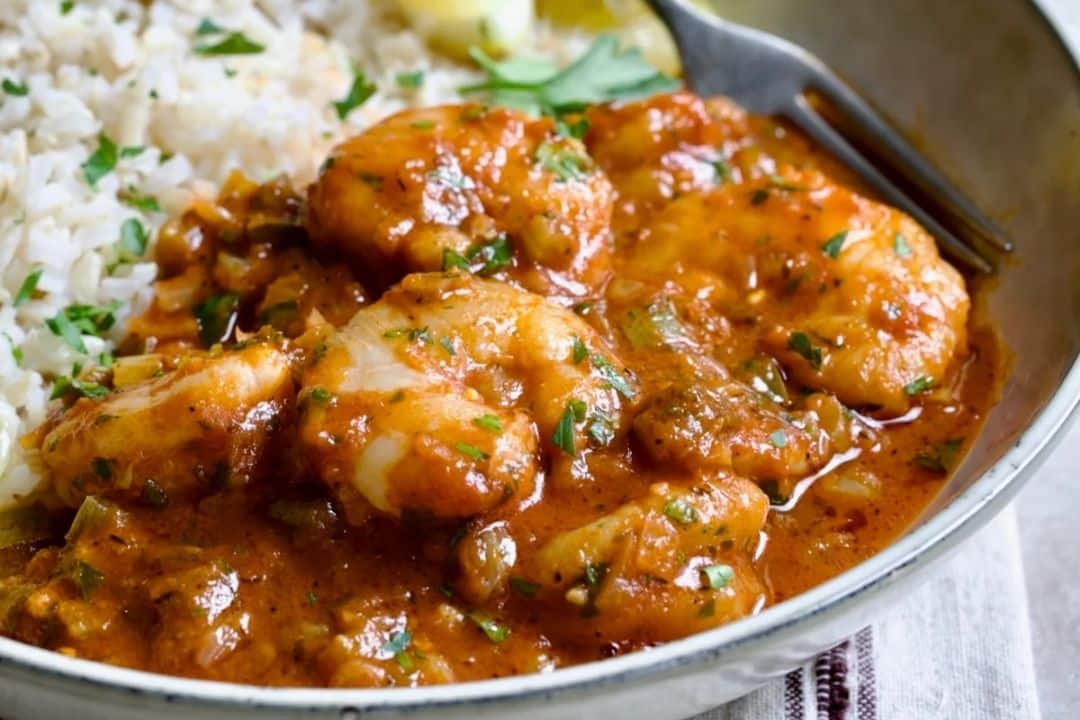Rice and chicken stew with tomato-based sauce and herbs, served in a bowl with a fork.