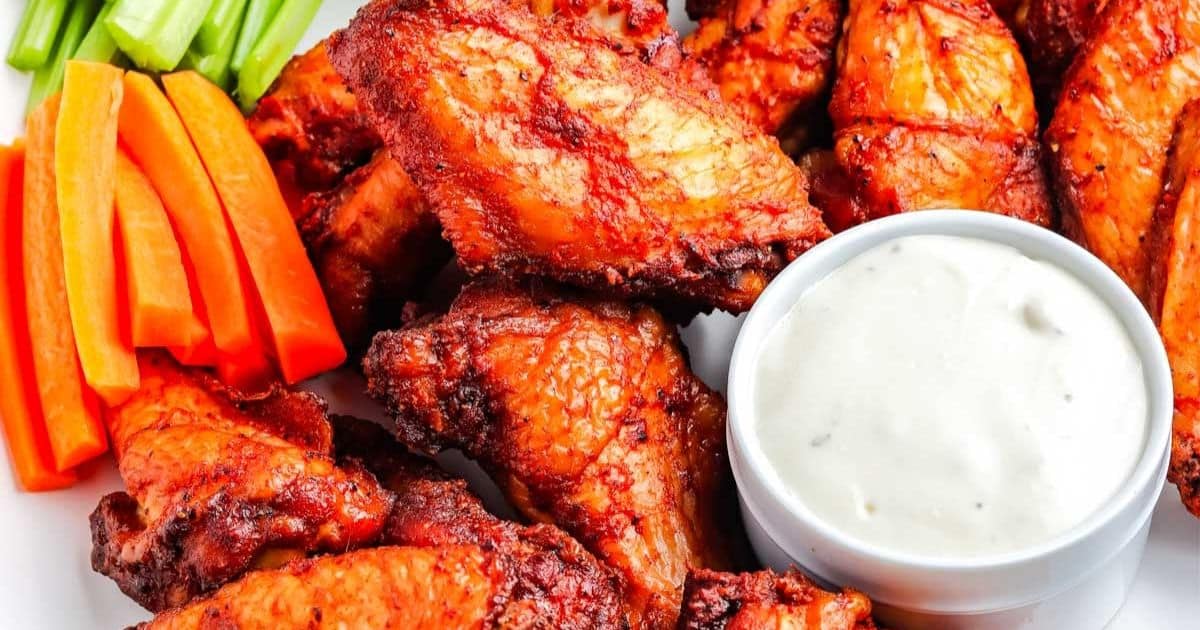 A plate of buffalo chicken wings with carrot, celery sticks, and a cup of ranch dipping sauce.