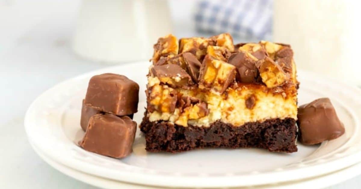 A slice of chocolate and caramel dessert topped with candy pieces, served with chocolate-covered candies on a plate.