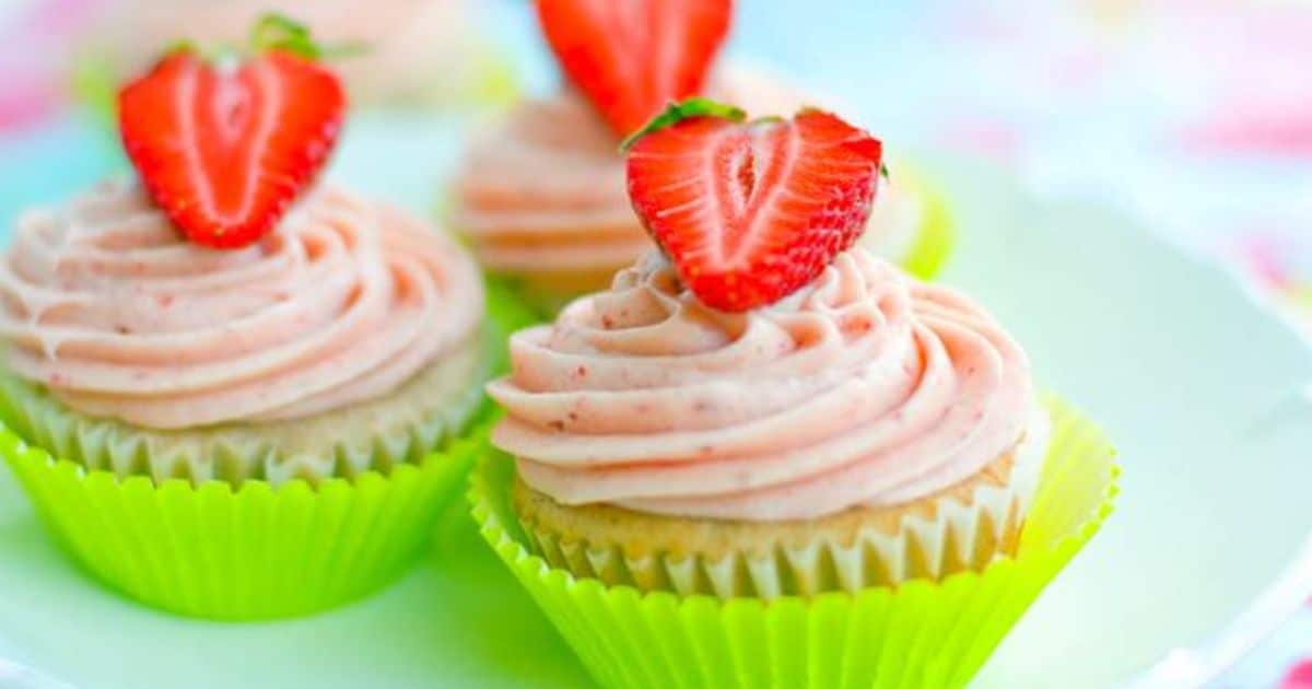 Cupcakes with pink frosting and half a strawberry on top, in green paper liners on a white plate.
