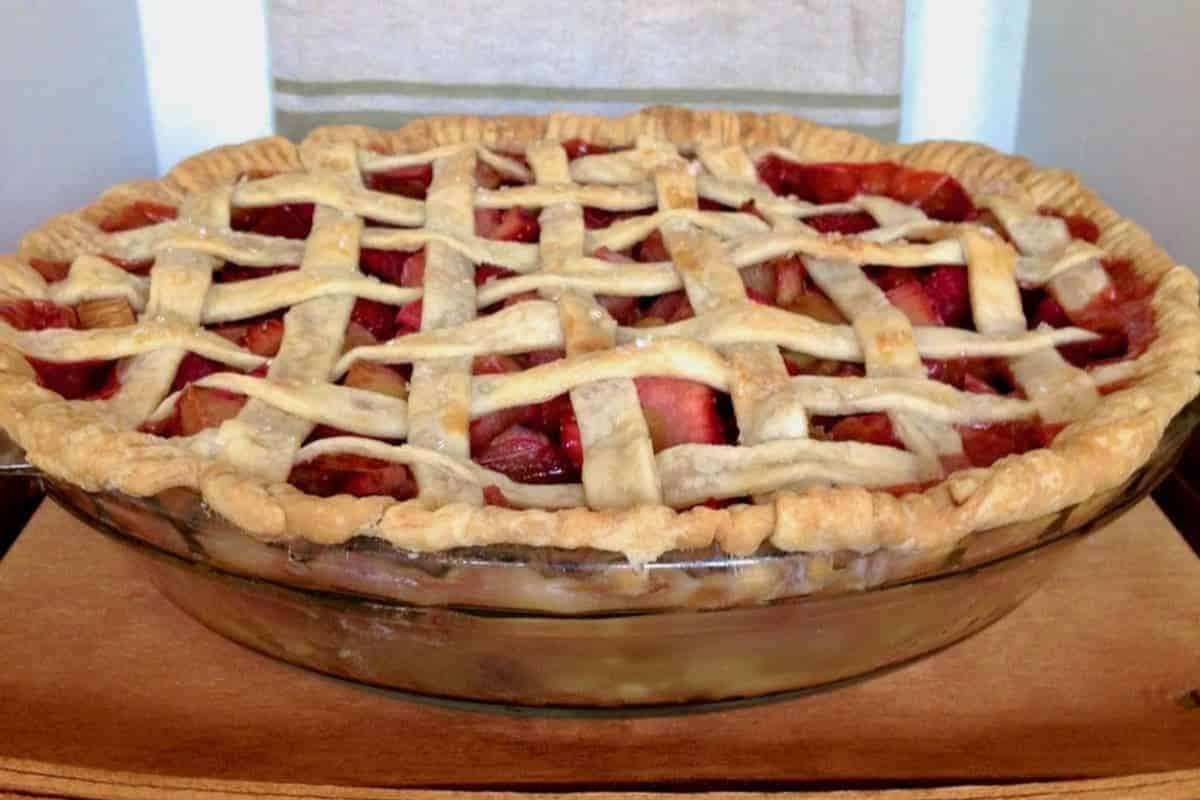 A baked fruit pie with a golden lattice crust in a clear glass pie dish.