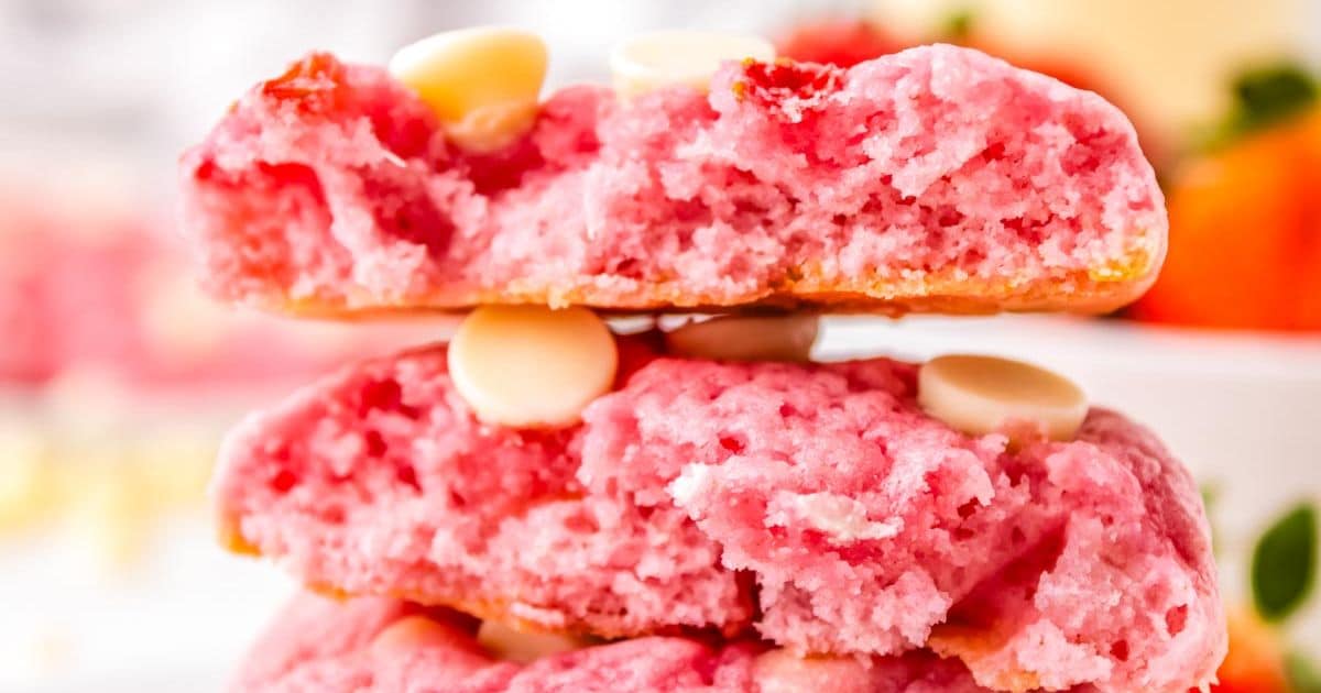 Close-up of two stacked, soft pink cookies with white chocolate chips and a blurred background.