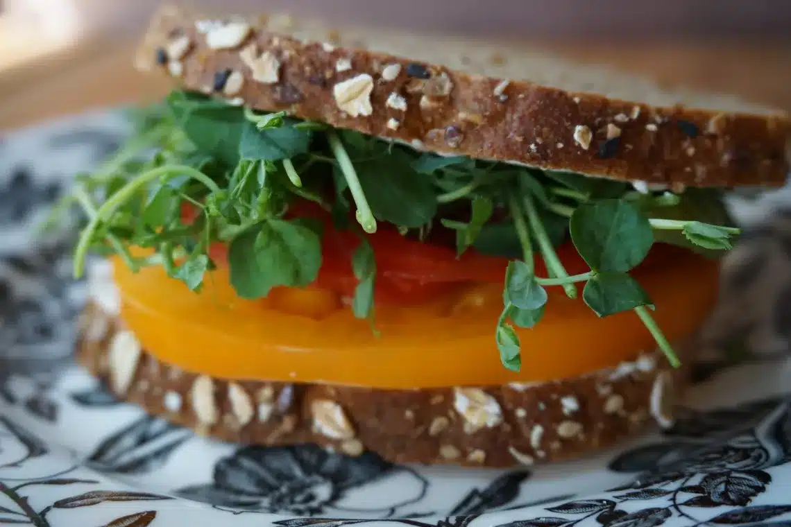 A sandwich with oat bread, yellow tomato, red tomato, and leafy greens on a floral plate.
