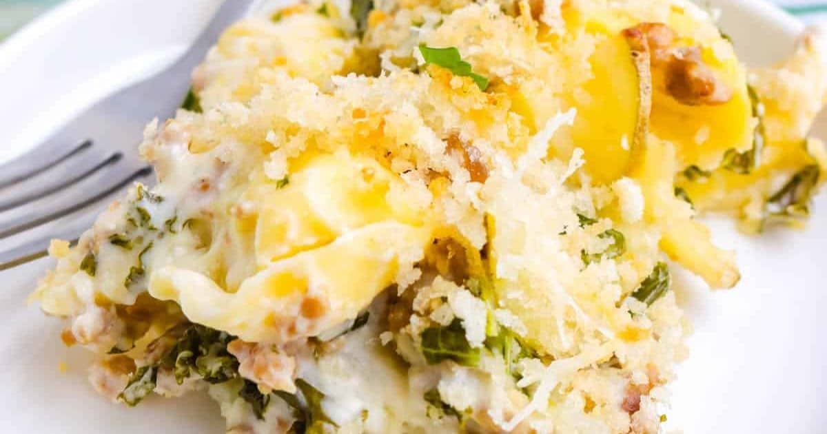 Baked cheesy casserole with breadcrumbs, greens, and pasta on a white plate with a fork.