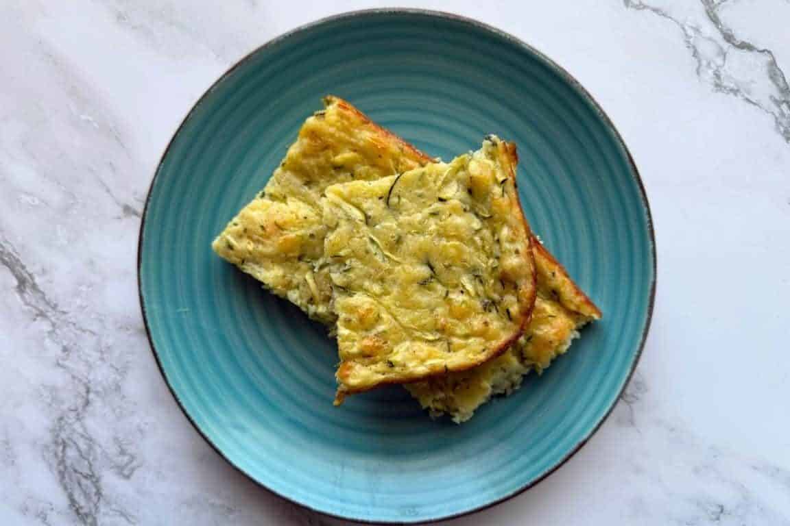 Two slices of zucchini casserole on a turquoise plate, placed on a marble surface.