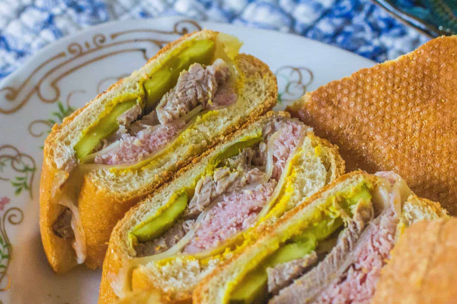 Close-up of a sliced Cuban sandwich with layers of meat, pickles, and cheese on a patterned plate.