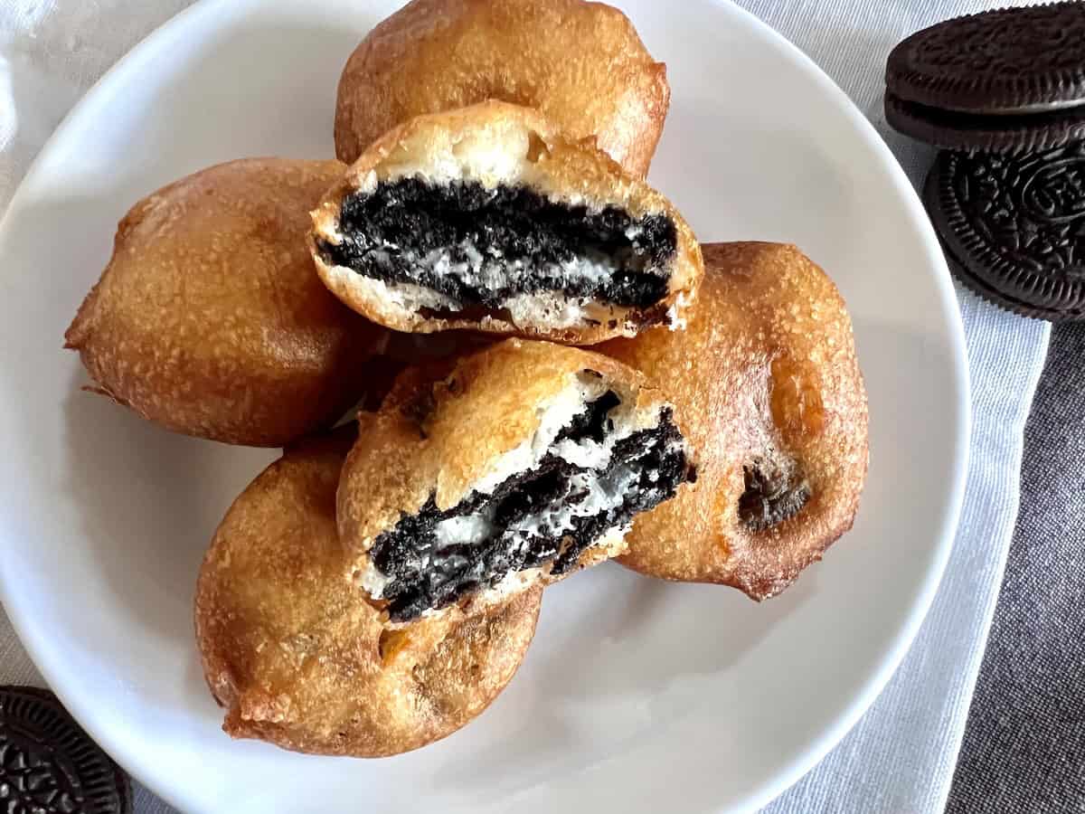 Four deep-fried Oreos on a white plate, two cut open showing the cream filling and chocolate cookie inside.