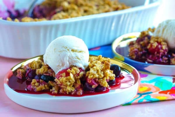 A serving of mixed berry crisp on a white serving plate with a scoop of ice cream on top.